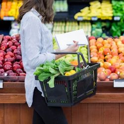 vrouw met boodschappenmand bij fruit in de supermarkt