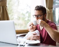 Man aan tafel met baby en laptop