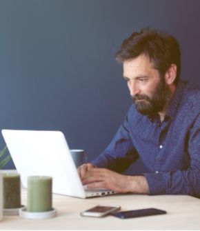 Man met baard zit voor een laptop, kijkt naar het scherm met zijn handen op het toetsenbord