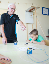 Techniekcoach geeft aanwijzingen aan kinderen met een batterij.